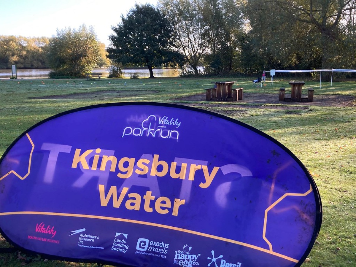 Kingsbury Water parkrun banner at the start area with lake and woodland in the background